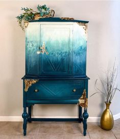 a blue and gold painted armoire next to a vase