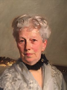 an old woman with white hair wearing a black collared shirt and gold earrings is looking at the camera