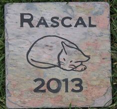 a stone with a drawing of a cat on it that says rascal 2013 in black ink