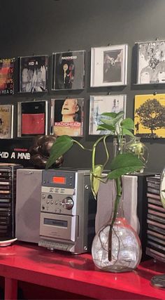 a red table topped with electronics and a vase filled with green plant sitting on top of it