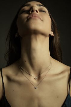 a woman with her eyes closed wearing a necklace and earring, looking up at the sky