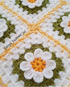 a crocheted blanket with white and green flowers on it's edges, in the shape of a flower