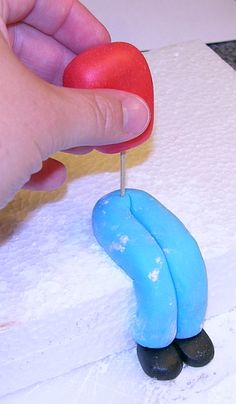 a hand holding a heart on top of a small blue figure with a red nose