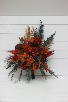 a bouquet of orange flowers and greenery on a white wooden wall with planks