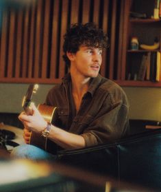 a young man sitting in a chair holding a guitar and looking at the camera with a smile on his face