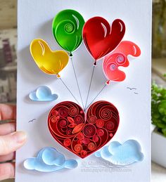 a hand holding a card with balloons in the shape of a heart