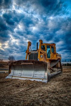 a yellow bulldozer sitting on top of a dirt field under a cloudy sky