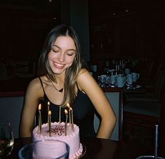 a woman sitting in front of a pink cake with lit candles