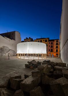 an empty courtyard with large rocks in the foreground and buildings in the background at night