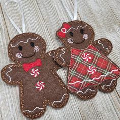 two gingerbread cookies are hanging from strings on a wooden surface, one has a red plaid bow tie and the other has a brown teddy bear