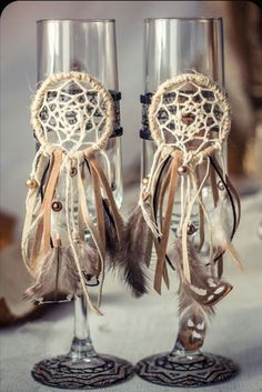 two wine glasses decorated with feathers and laces are sitting next to each other on a table