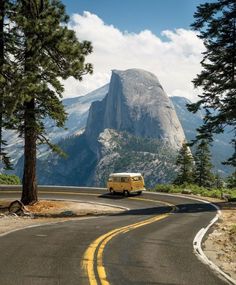 a van driving down the road in front of a mountain with trees on both sides