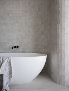 a white bath tub sitting in a bathroom next to a wall covered in grey tiles