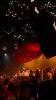 a large group of people sitting in front of a stage with red balloons floating from the ceiling