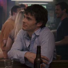 a man sitting at a table with a beer in front of him and people behind him