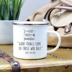 a white coffee mug sitting on top of a wooden table next to a purse and potted plant