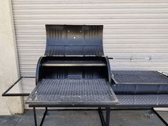 two barbecue grills sitting next to each other on top of a metal table in front of a garage door