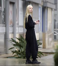 a blonde woman with long hair is standing on the sidewalk