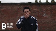 a man covers his mouth with his hands as he stands in front of a brick wall