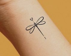 a small black dragonfly tattoo on the left inner arm and wrist, with a heart in the middle