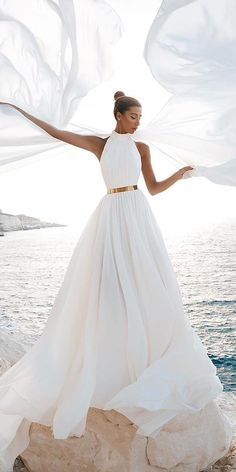 a woman standing on top of a rock next to the ocean wearing a white dress