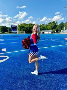 a cheerleader is posing on the field with her pom - poms in hand