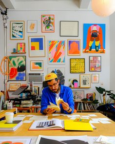 a man sitting at a table reading a book in front of pictures on the wall