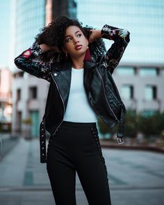 a woman in black pants and a white top is posing with her hands on her head