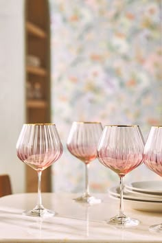 four pink wine glasses sitting on top of a table next to plates and utensils