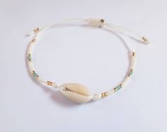 a white beaded bracelet with a shell and beads on the end, sitting on a white surface