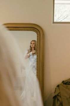 a woman in a wedding dress looking at herself in the mirror