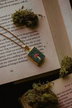 two necklaces sitting on top of an open book with moss growing out of it