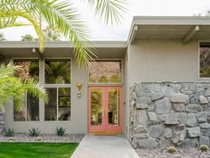 a house with a pink door and palm trees in front of the entrance to it