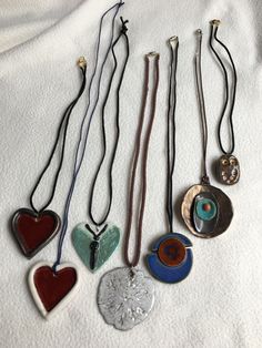 five necklaces with different shapes and colors on white cloth background, including one heart shaped pendant