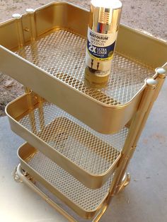 a gold metal cart with two shelves and a spray bottle on the bottom one shelf