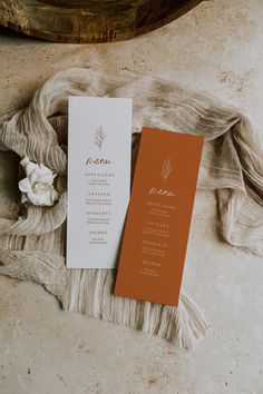 an orange and white menu sitting on top of a table next to a piece of cloth