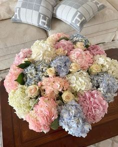 a bouquet of flowers sitting on top of a wooden table next to two gray and white pillows