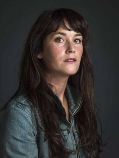 a woman with long dark hair wearing a denim jacket and looking off to the side