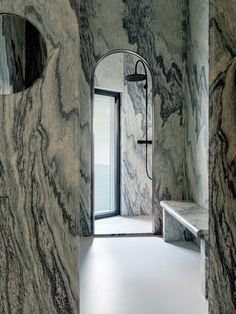 a bathroom with marble walls and flooring next to a doorway that has a bench in front of it