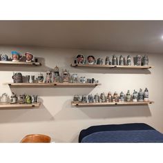 three wooden shelves filled with cups and mugs on top of a wall next to a bed