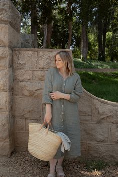 a woman standing next to a stone wall holding a wicker basket and looking off into the distance