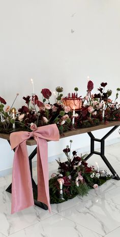 an arrangement of flowers and candles on a table with pink ribbon tied around the edge