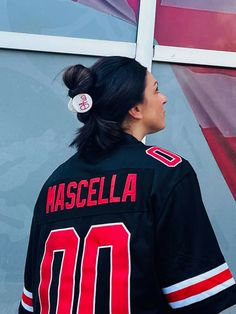 a woman wearing a black jersey with red and white stripes on the back, standing in front of a wall