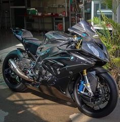 a black motorcycle parked in front of a building next to a palm tree and potted plant