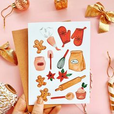 a hand holding up a card with christmas items on it and gold decorations around it