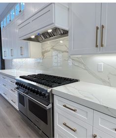 a kitchen with white cabinets and marble counter tops, along with stainless steel oven hoods