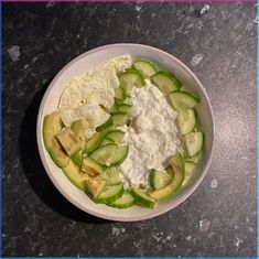 a white bowl filled with cucumbers and cheese on top of a black table