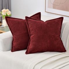 two red pillows sitting on top of a white couch next to a vase with flowers