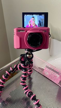 a pink camera sitting on top of a tripod in front of a laptop computer