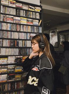 a young woman wearing headphones standing in front of a book shelf filled with dvds